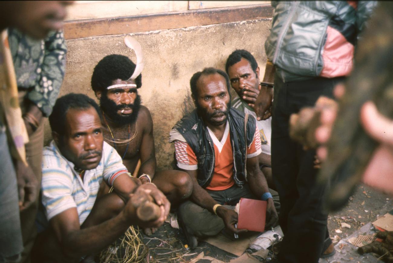 BD/166/282 -
Papua men in western and traditional cloths sitting against a wall