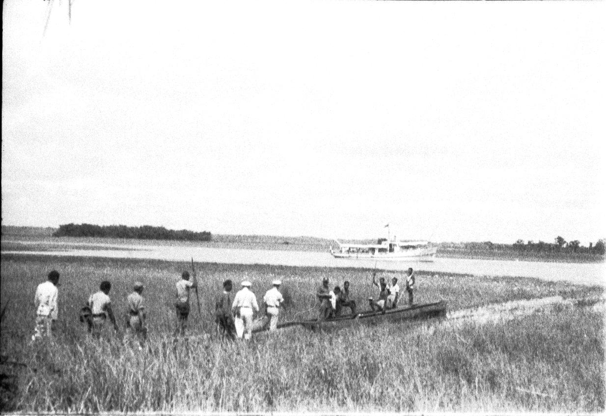 BD/67/235 - 
People on the road crossing water with reed
