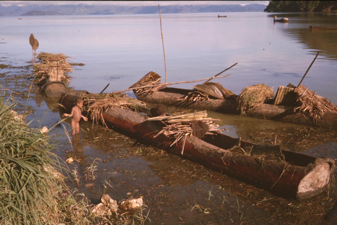 BD/132/170 -
jongen naast drie prauwen met houttrossen in water
