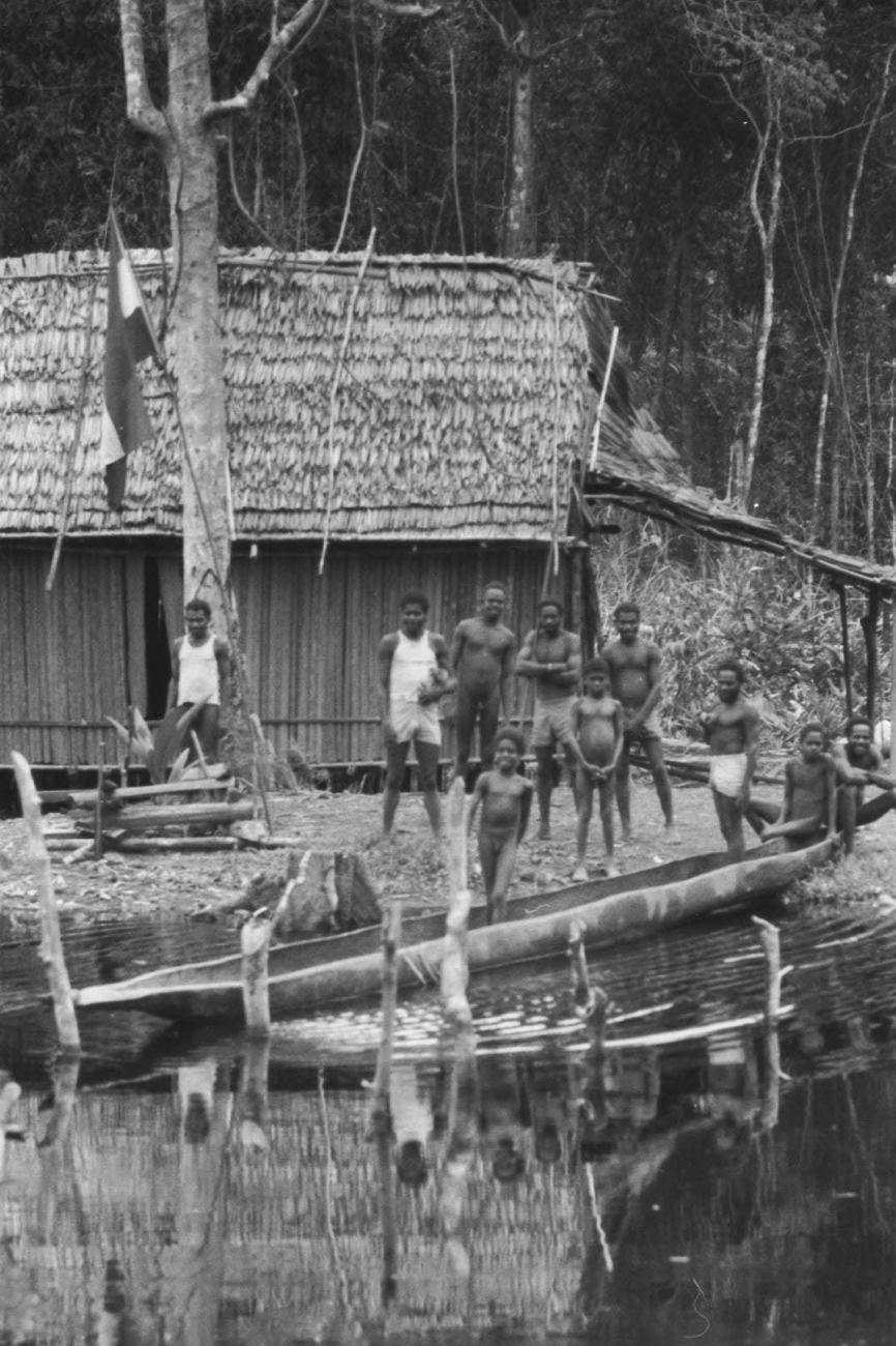 BD/133/52 -
Tocht Merauke-Kapi: Marind-anim mensen staande bij een huis aan de oever