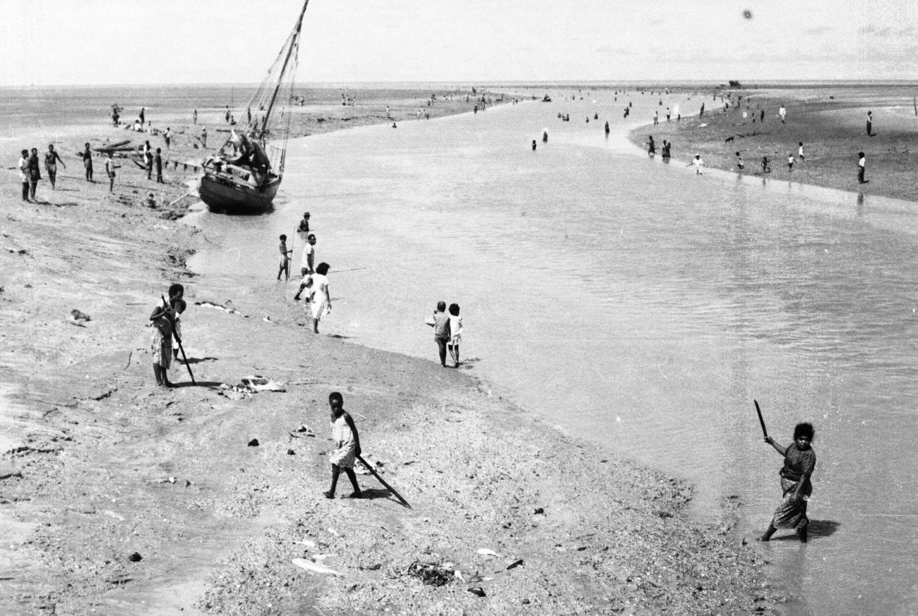 BD/133/949 - 
Getijdelandschap met met drooggevallen zeilschip en langs de oevers vissende Papoea&#039;s 
