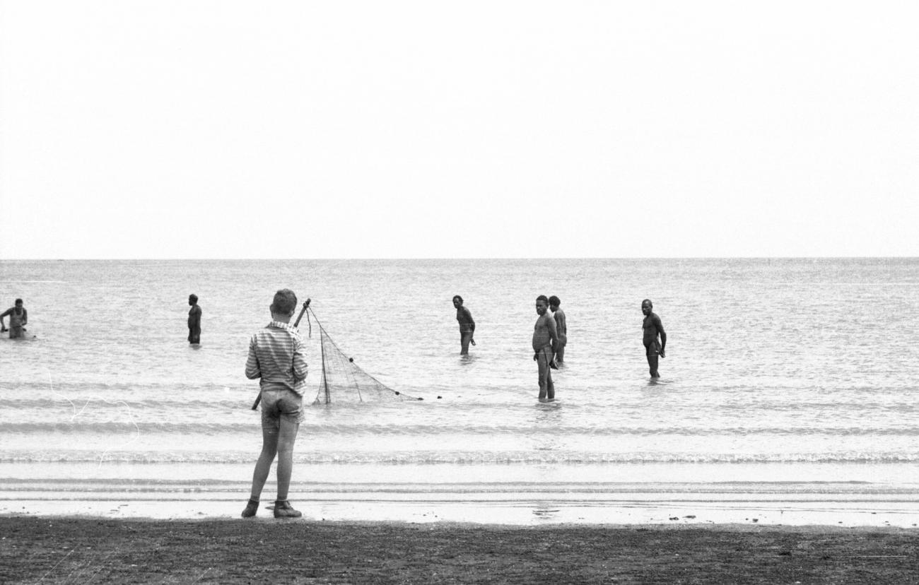 BD/133/983 - 
Groep Papoea&#039;s zet een visnet uit in het water, met op de voorgrond een westerse jongen
