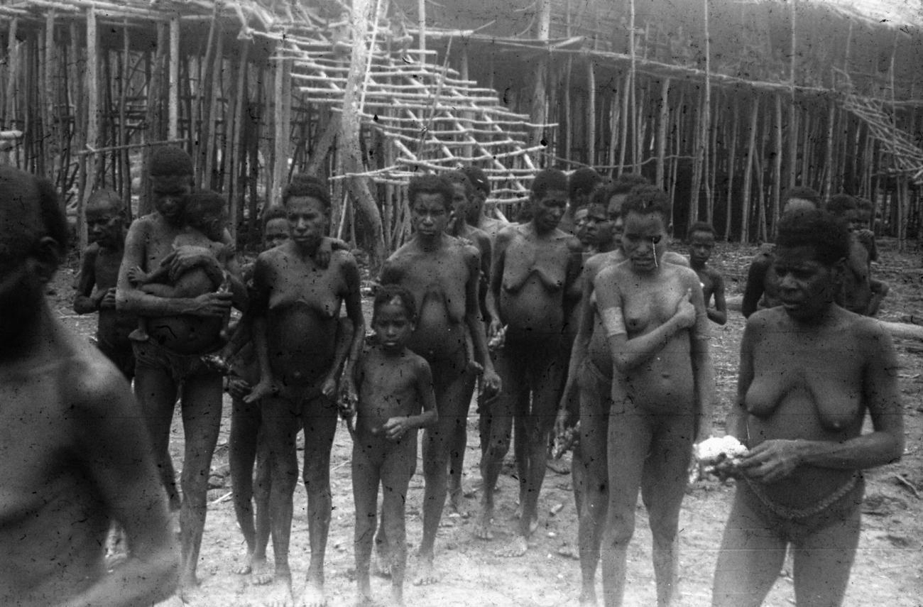 BD/216/55 - 
Vrouwen en kinderen uit de Asmat voor huis op palen
