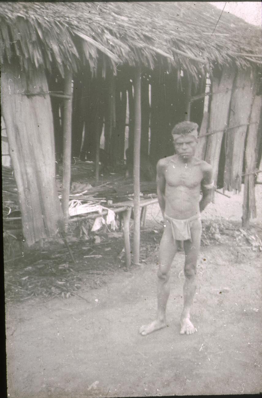 BD/309/193 -
Man poserend voor de ingang van een lage paalwoning
