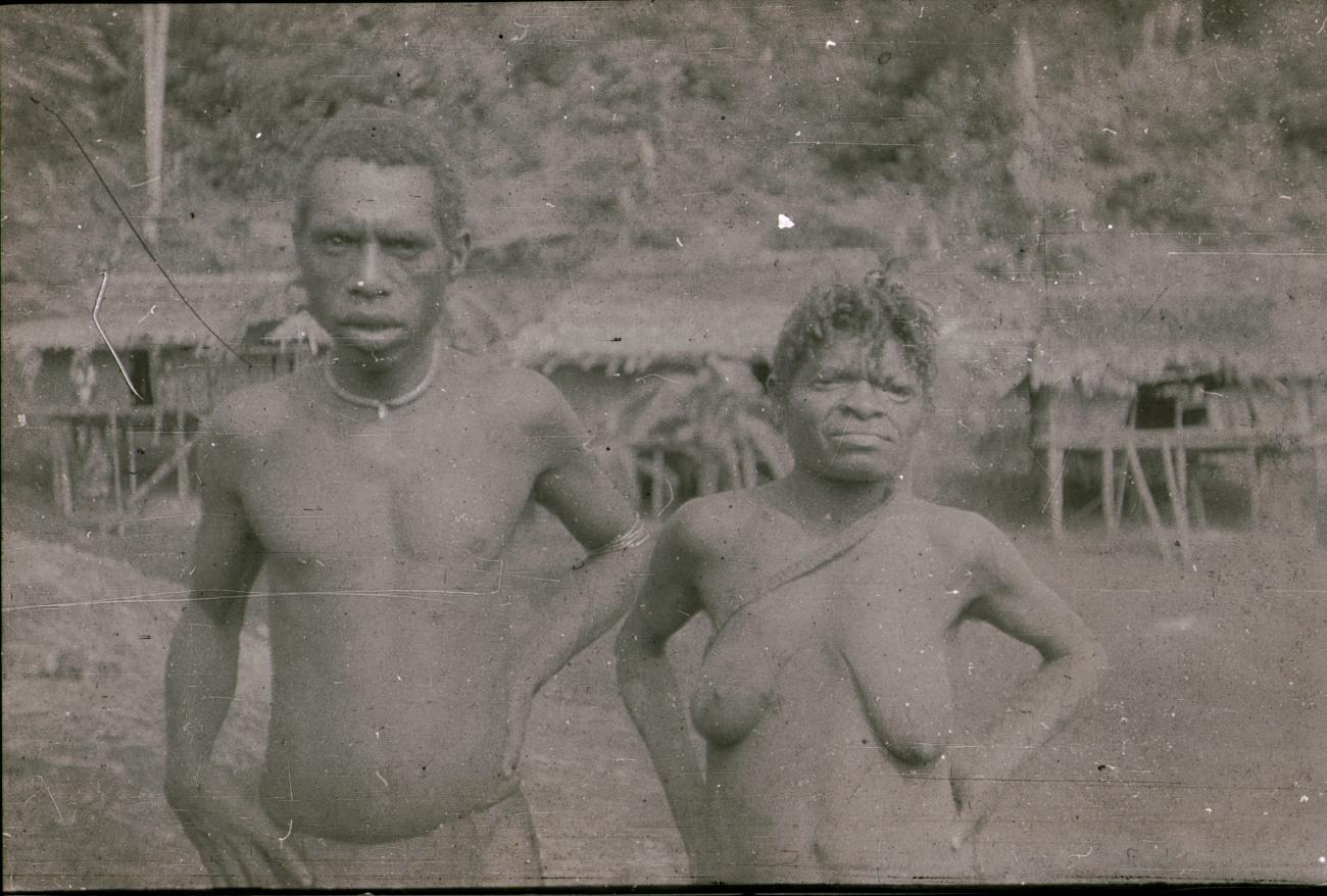 BD/309/194 -
Man en vrouw met op de achtergrond traditionele paalwoningen