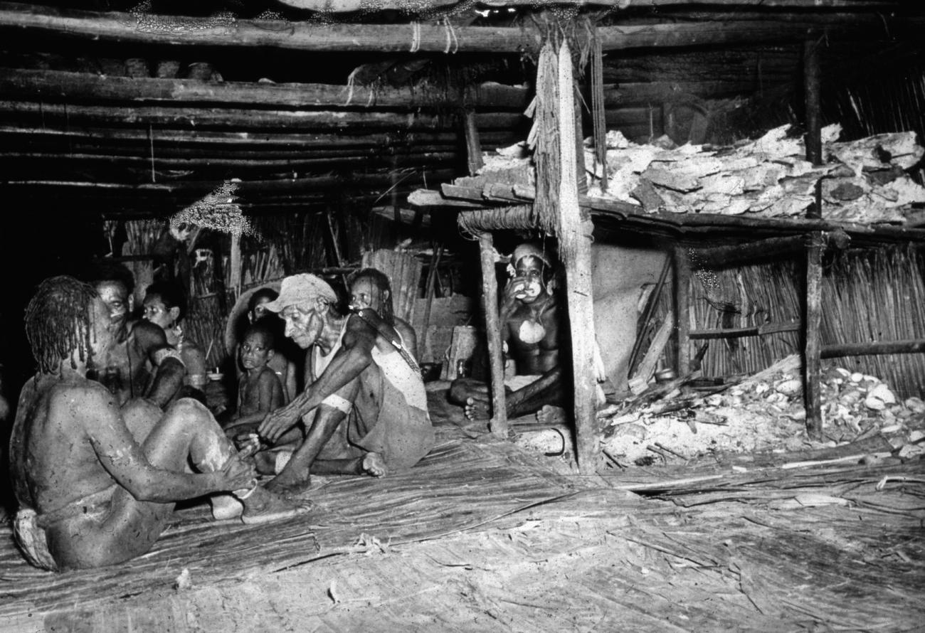 BD/66/185 - 
Asmat,mannen en jongens zitten in het mannenhuis
