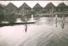 BD/309/351 Paalwoningen aan de rivier waarin twee prauwen in het dorp Kasueri
